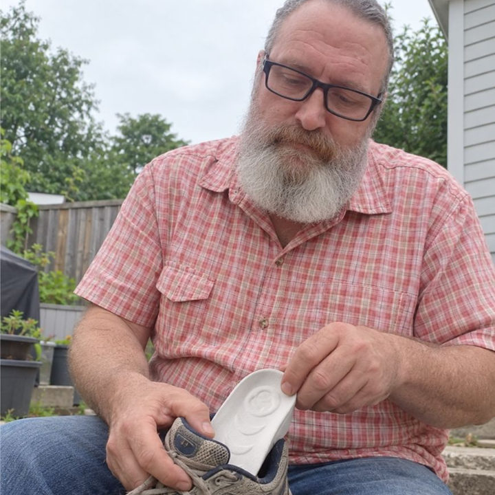 Man fitting a white HighPads insert into a worn walking shoe outdoors